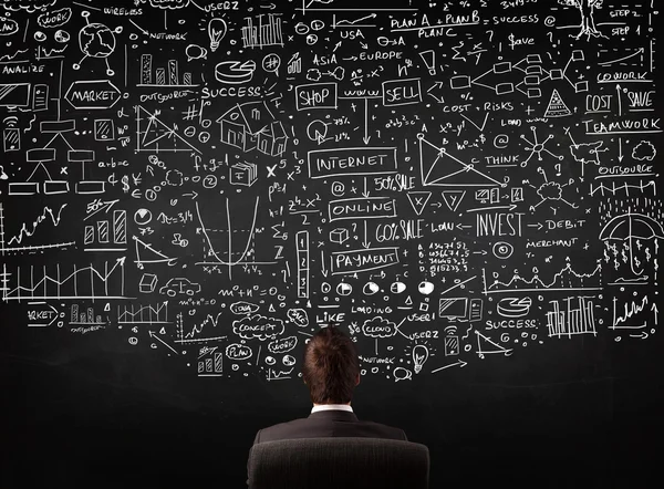 Businessman sitting in front of a blackboard with charts — Stock Photo, Image