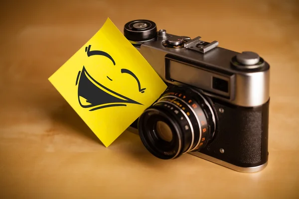 Post-it note with smiley face sticked on photo camera — Stock Photo, Image