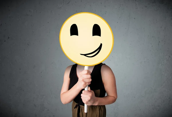 Young woman holding a smiley face emoticon — Stock Photo, Image