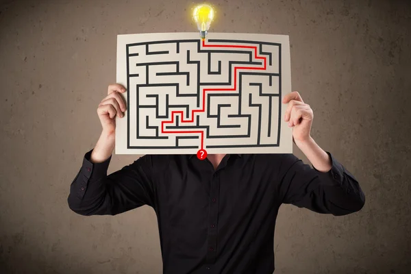 Businessman holding a paper with a labyrinth on it in front of h — Stock Photo, Image