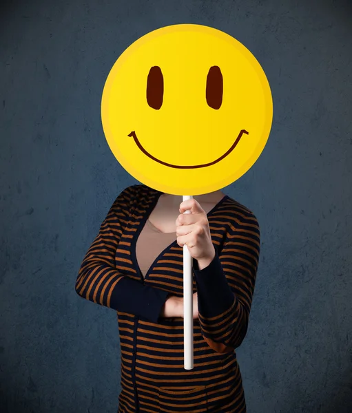 Young woman holding a smiley face emoticon — Stock Photo, Image