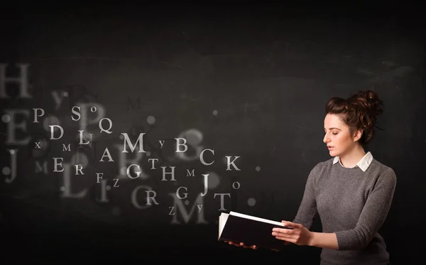 Jovencita leyendo un libro con letras del alfabeto — Foto de Stock