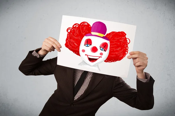 Businessman holding a cardboard with a clown on it in front of h — Stock Photo, Image