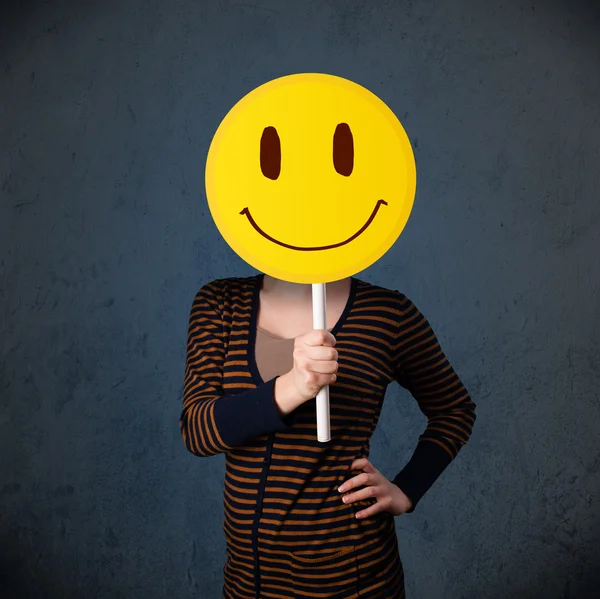 Young woman holding a smiley face emoticon — Stock Photo, Image