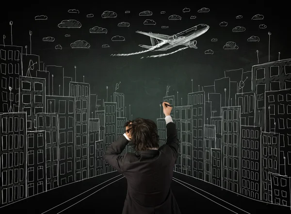 Businessman sitting in front of a cityscape drawing on a chalkbo — Stock Photo, Image