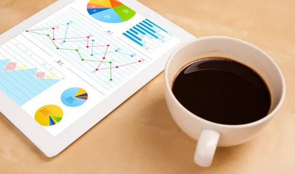 Tablet bilgisayarı ekranda çizelgeleri ve masada bir fincan kahveyi gösteriyor. — Stok fotoğraf