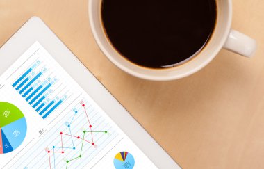 Tablet bilgisayarı ekranda çizelgeleri ve masada bir fincan kahveyi gösteriyor.