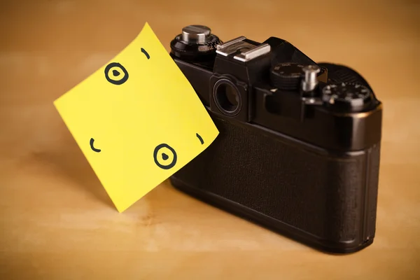 Nota post-it con la cara sonriente pegada a una cámara fotográfica — Foto de Stock