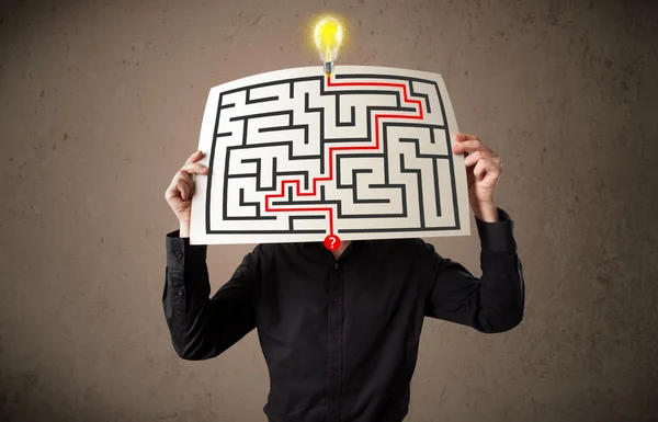 Businessman holding a paper with a labyrinth on it in front of h — Stock Photo, Image