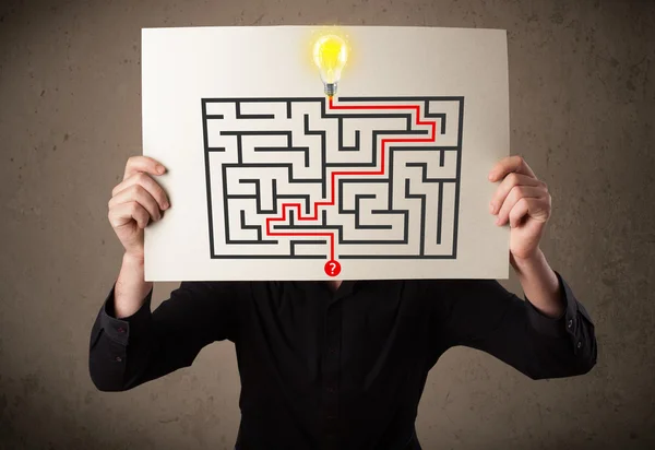 Businessman holding a paper with a labyrinth on it in front of h — Stock Photo, Image