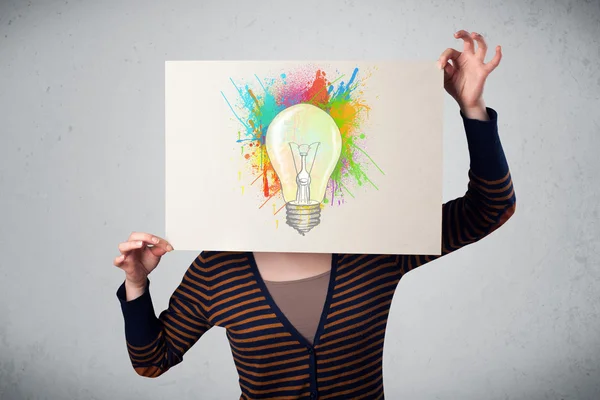 Woman holding a cardboard with paint splashes and lightbulb in f — Stock Photo, Image