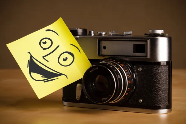 Nota pós-it com rosto sorridente colado na câmera fotográfica — Fotografia de Stock