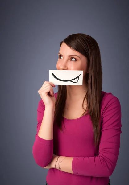 Pretty young girl holding white card with smile drawing — Stock Photo, Image