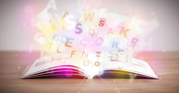 Aufgeschlagenes Buch mit leuchtenden Buchstaben auf Betongrund — Stockfoto