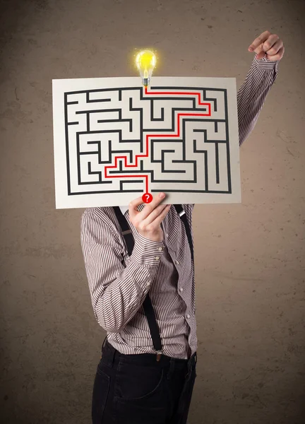 Businessman holding a paper with a labyrinth on it in front of h — Stock Photo, Image