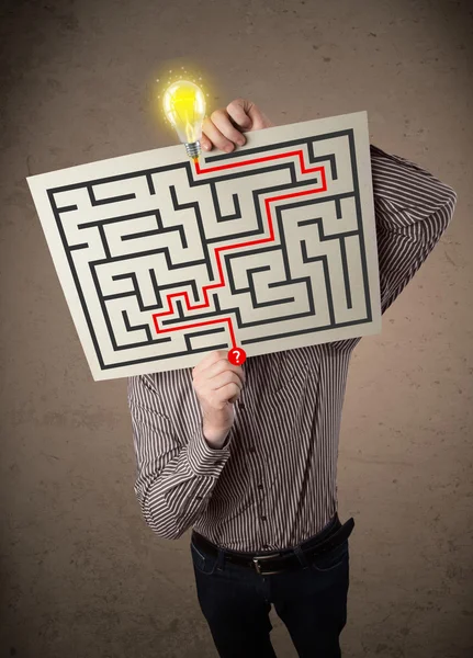 Empresário segurando um papel com um labirinto na frente de h — Fotografia de Stock