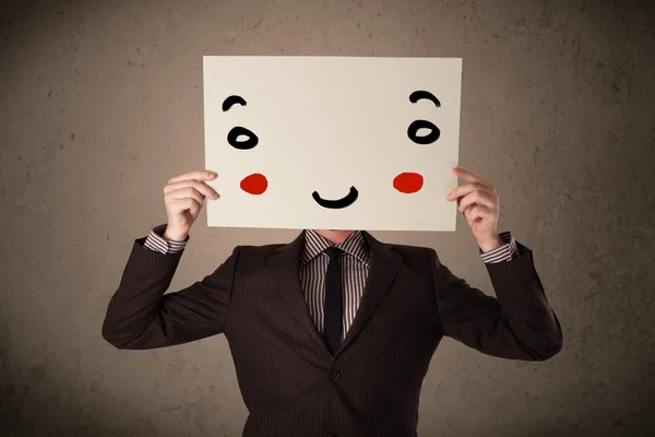 Businessman holding a cardboard with a smiley face on it — Stock Photo, Image