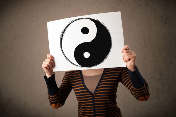 Woman holding a paper with a yin-yang on it in front of her head — Stock Photo, Image