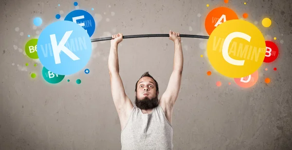 Skinny guy lifting colorful vitamin weights — Stock Photo, Image