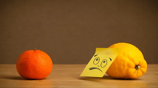 Лимон с липкой запиской, печально смотрящий на оранжевый — стоковое фото