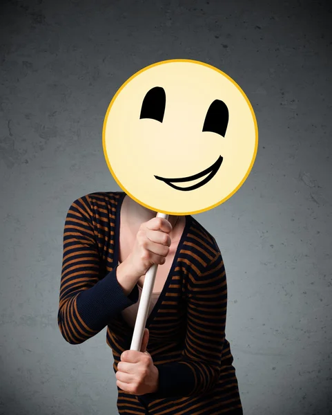 Young woman holding a smiley face emoticon — Stock Photo, Image