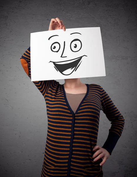 Женщина, держащая картон с улыбающимся лицом перед собой — стоковое фото