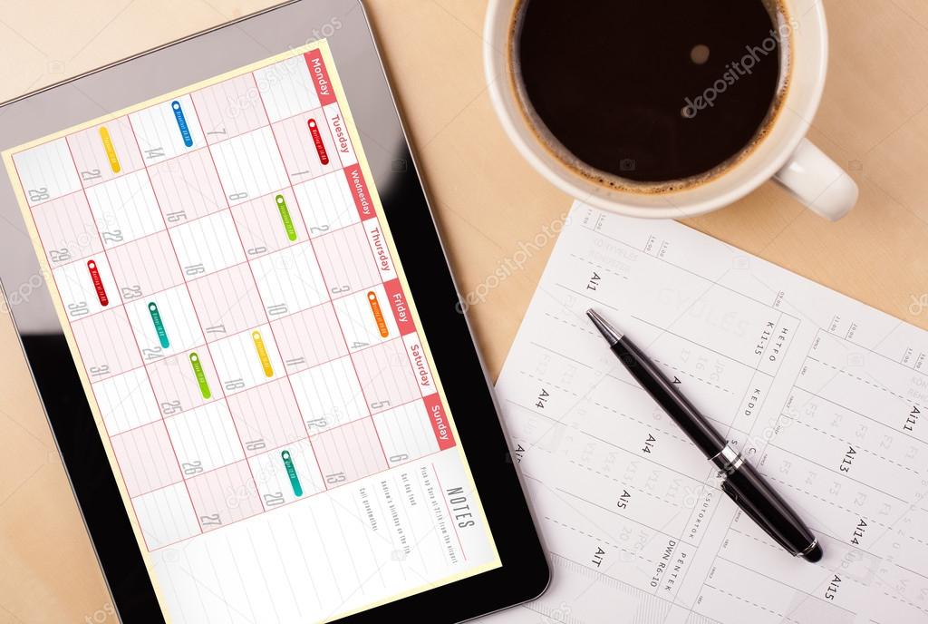 Tablet pc showing calendar on screen with a cup of coffee on a d