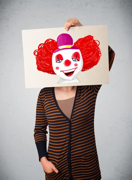 Woman holding a cardboard with a clown on it in front of her hea — Stock Photo, Image