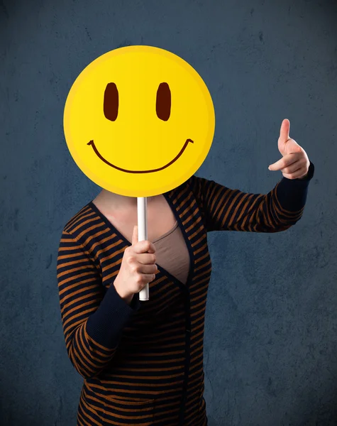 Young woman holding a smiley face emoticon — Stock Photo, Image