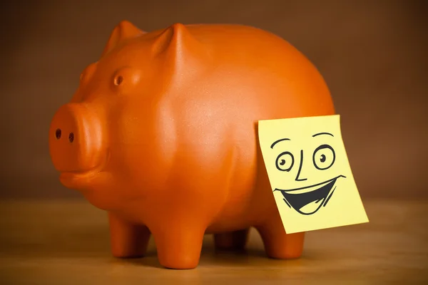 Post-it note with smiley face sticked on a piggy bank — Stock Photo, Image