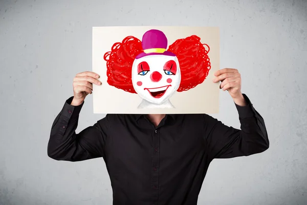 Businessman holding a cardboard with a clown on it in front of h — Stock Photo, Image