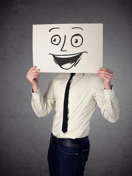 Empresário segurando um papelão com rosto sorridente na frente — Fotografia de Stock