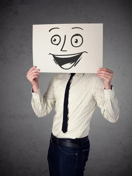 Empresario sosteniendo una cartulina con cara sonriente en él en frente — Stok fotoğraf