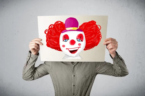 Businessman holding a cardboard with a clown on it in front of h — Stock Photo, Image