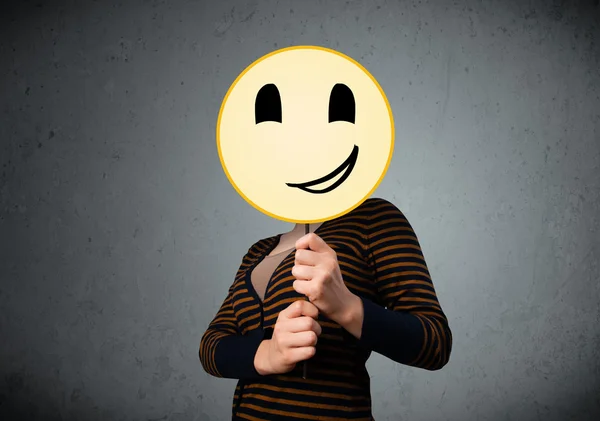 Young woman holding a smiley face emoticon — Stock Photo, Image