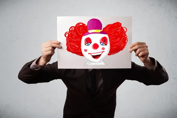 Businessman holding a cardboard with a clown on it in front of h — Stock Photo, Image