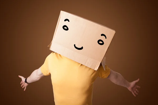 Young man gesturing with a cardboard box on his head with smiley — Stock Photo, Image