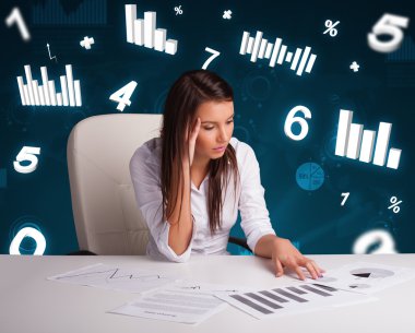 Masasında şema ve istatistiklerle oturan genç iş kadını.