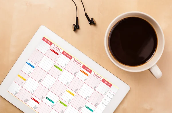 Tablet pc che mostra il calendario sullo schermo con una tazza di caffè su un d — Foto Stock