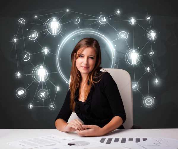 Businesswoman sitting at desk with social network icons — Stock Photo, Image