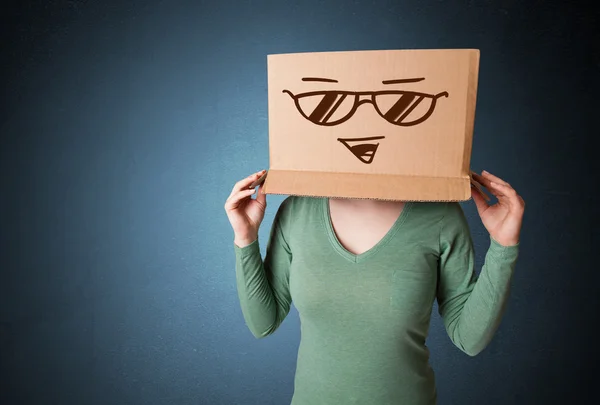 Jeune femme gestuelle avec une boîte en carton sur la tête avec le sourire — Photo