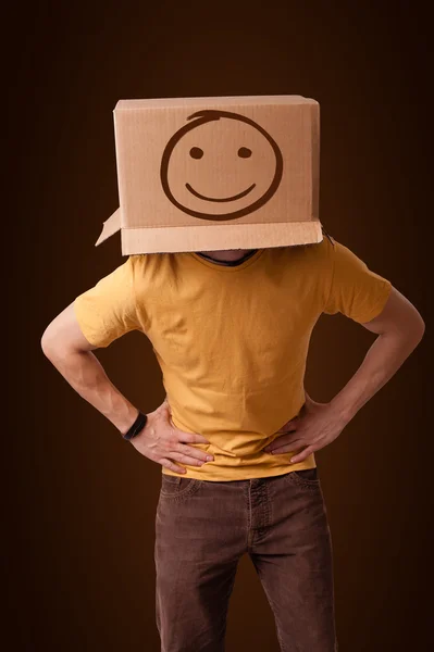 Young man gesturing with a cardboard box on his head with smiley — Stock Photo, Image