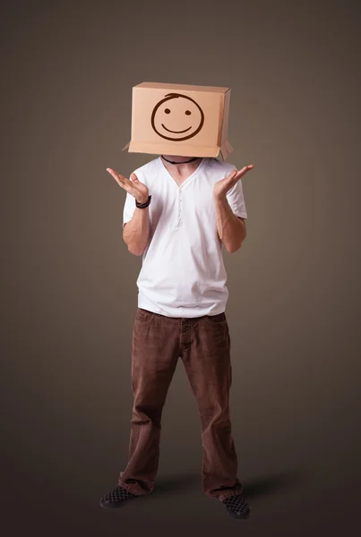 Ung man gestikulerande med en kartong på hans huvud med smiley — Stockfoto