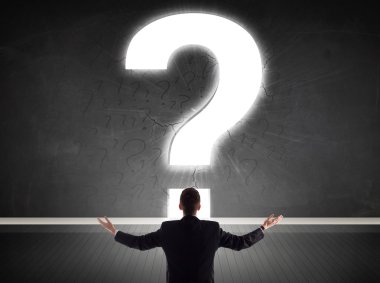 Parlak bir soru işaretiyle duvara bakan bir iş adamı 