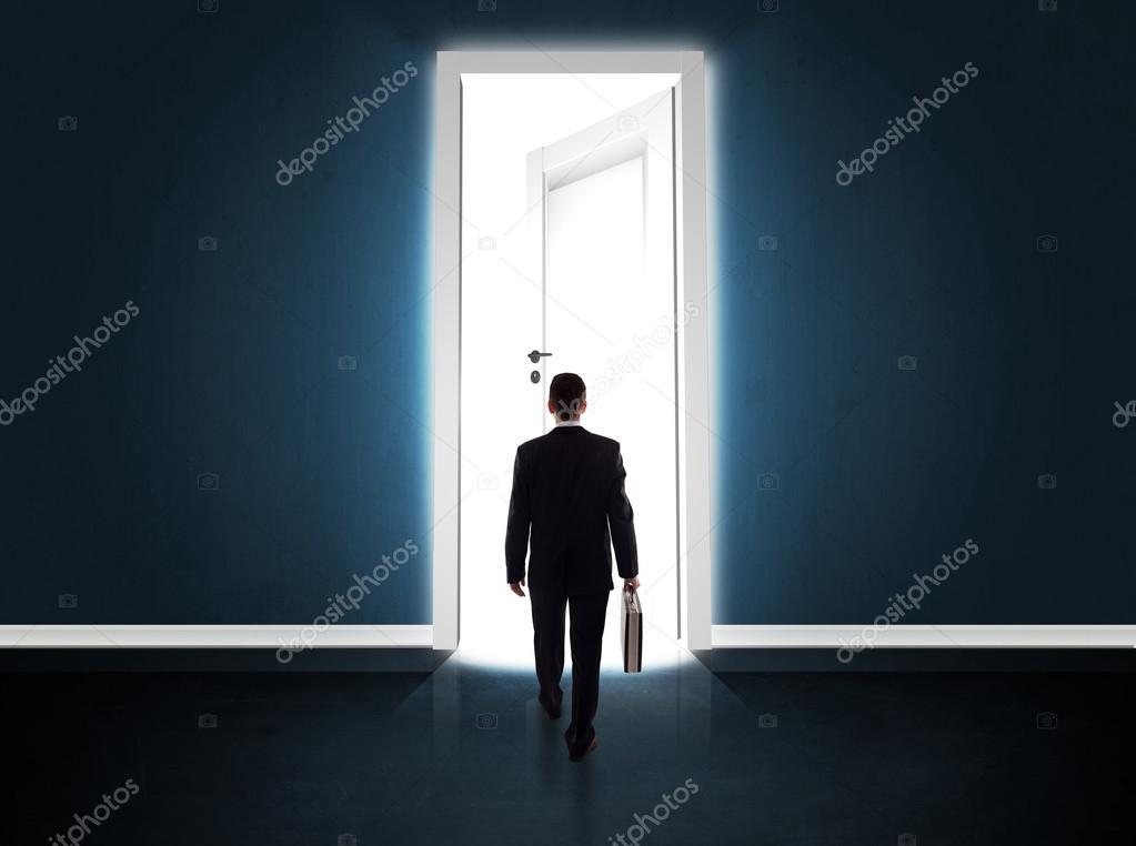 Business man looking at big bright opened door