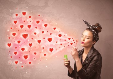 Güzel genç kız kırmızı kalp sembolleri üflüyor. 