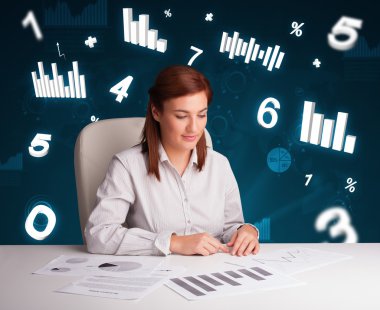Masasında şema ve istatistiklerle oturan genç iş kadını.
