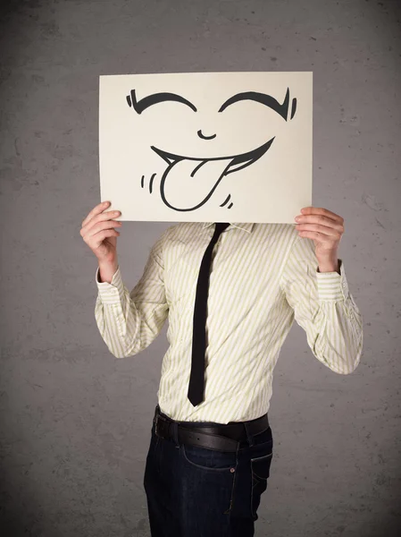 Businessman holding a paper with funny smiley face in front of h — Stock Photo, Image