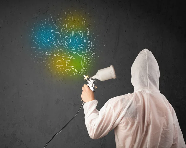 Worker with airbrush gun paints colorful lines and splashes — Stock Photo, Image