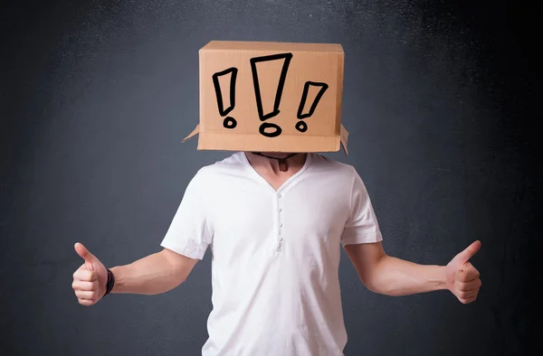 Young man gesturing with a cardboard box on his head with exclam — Stock Photo, Image